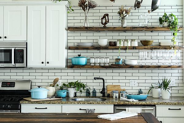 A kitchen counter is shown, above which minimalist shelves hold a variety of kitchen items in reusable containers