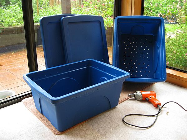 Two blue plastic bins and lids with holes drilled in the bottoms and sides.