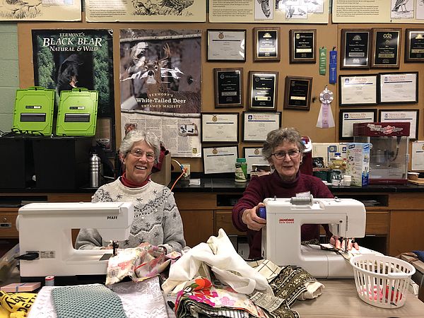 Volunteers with Sewing for Change smile behind their sewing machines.