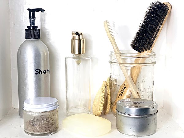 reusable shampoo bottle and lotion jar stand on a counter next to a glass jar holding a wooden hairbrush and toothbrush
