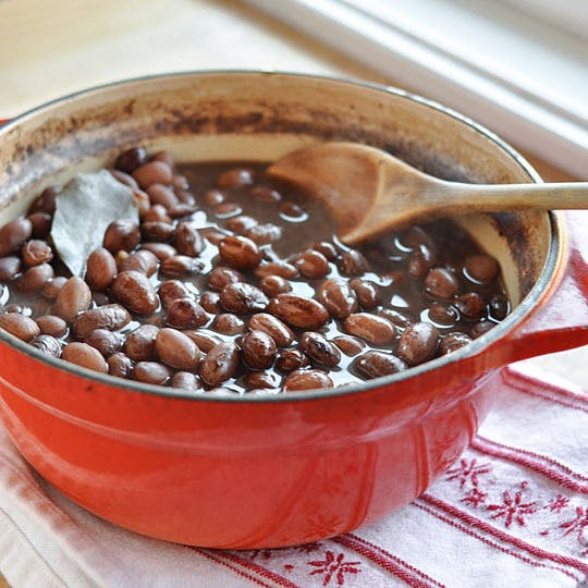 cooked beans in a ceramic pot with wooden spoon